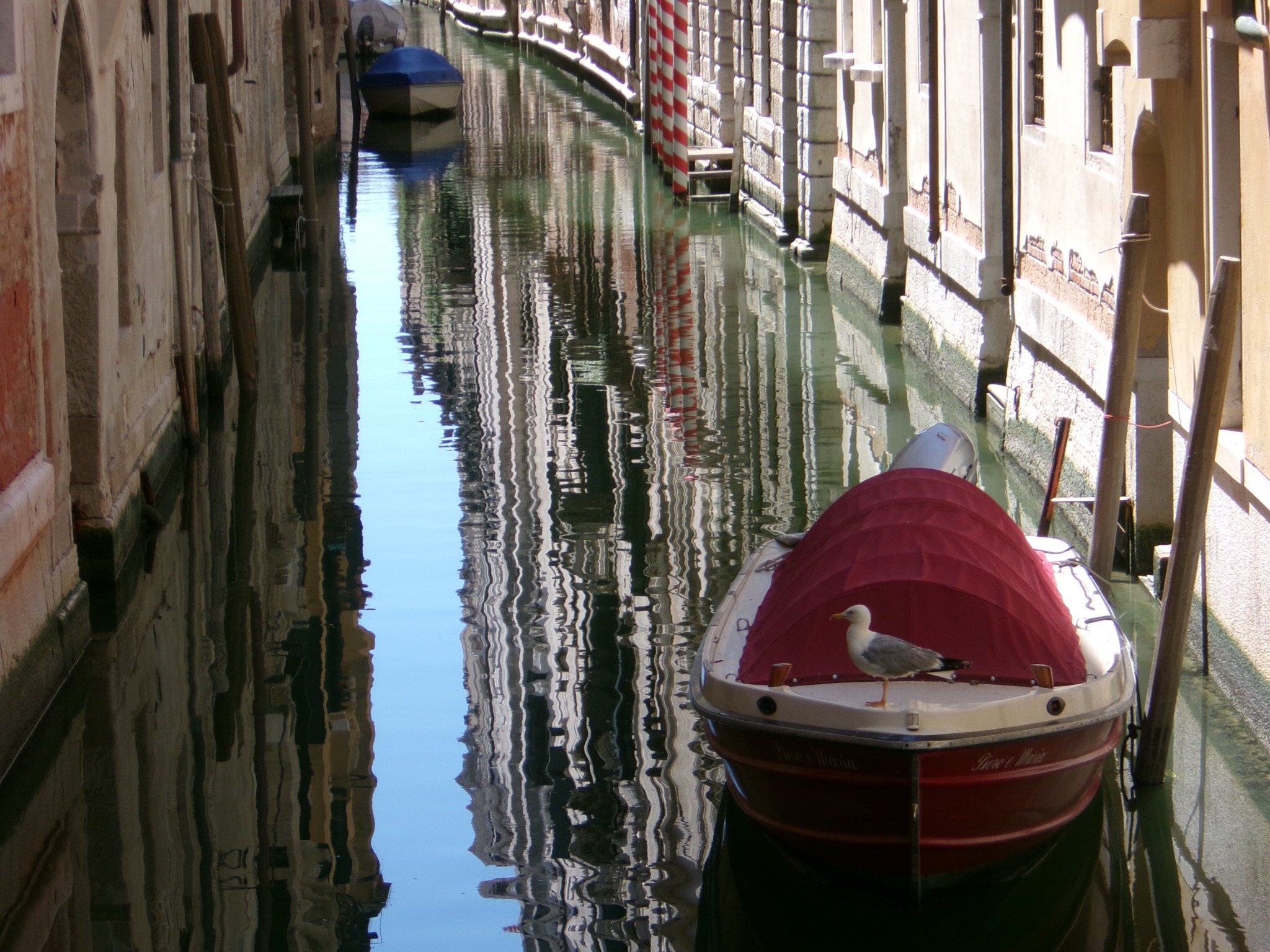 A red boat moored on a narrow canal with reflections