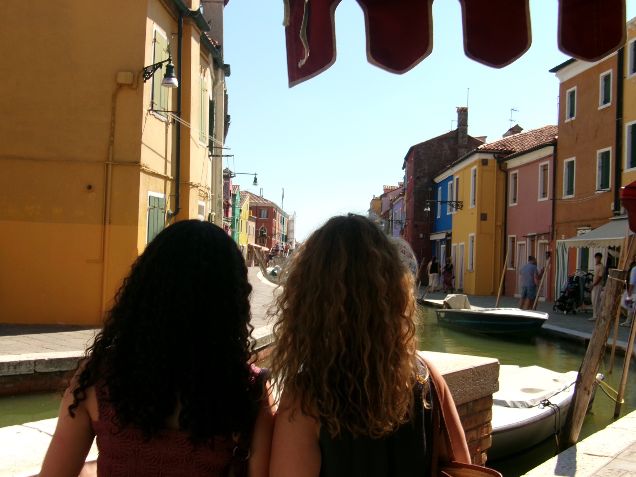 Two figures looking toward colorful houses beside a canal