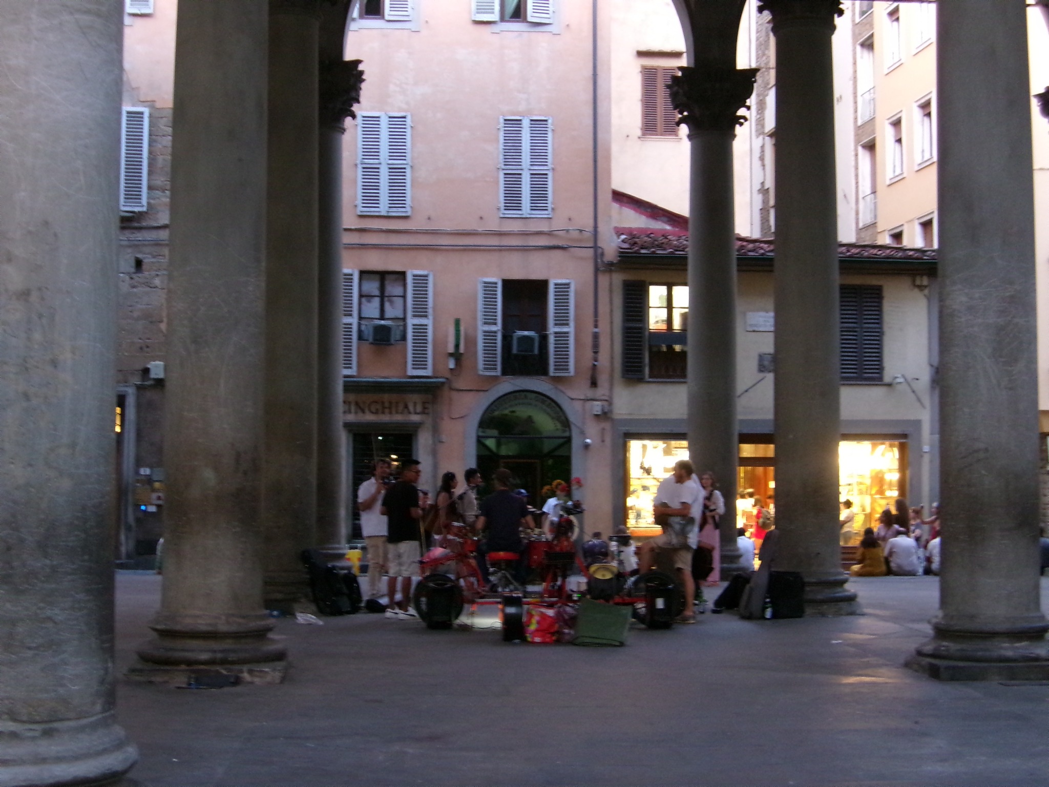 Musicians gathered among stone columns in a square at dusk