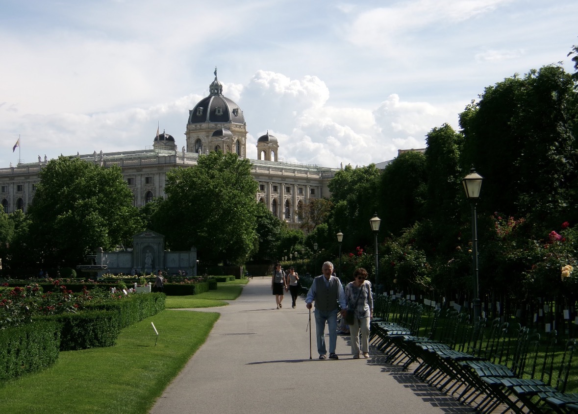 Two people walking through a formal garden beneath an ornate domed building