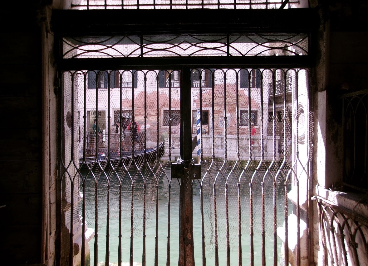 View through a metal gate toward buildings across a canal