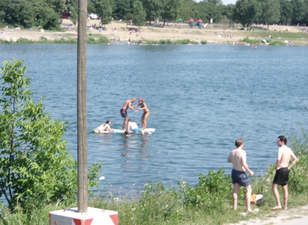 People enjoying blue water beside a green riverbank